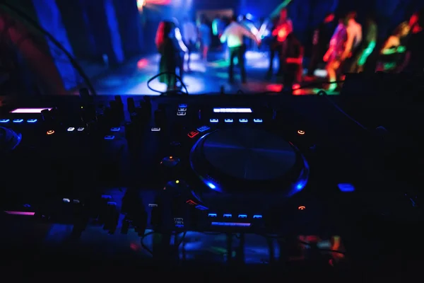 Verschwommene Menschen tanzen auf der Tanzfläche eines Nachtclubs mit DJ-Mischpult vor, um die Musik zu steuern — Stockfoto