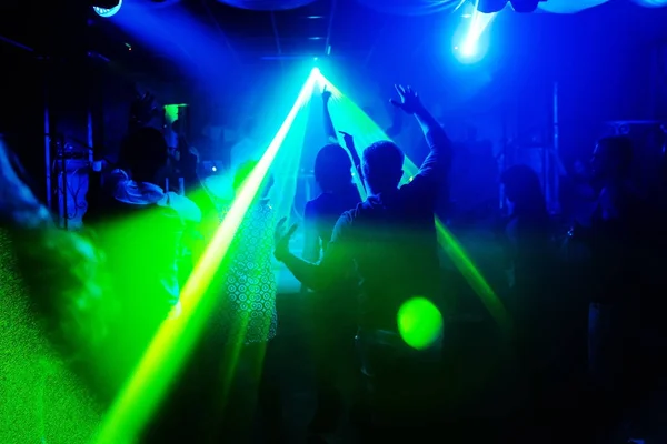 Sagome sfocate di persone con le mani alzate con la luce laser in discoteca — Foto Stock