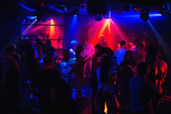 Wazig silhouetten van mensen dansen in de nachtclub onder kleurrijke schijnwerpers — Stockfoto