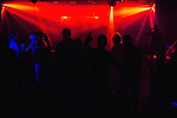 people silhouettes on dance floor of night club at the concert under red spotlights