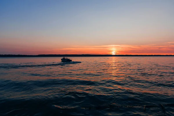 Barco flutua em ondas de água no fundo do pôr-do-sol vermelho e azul com sol — Fotografia de Stock