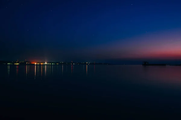 Stadt am Ufer von Fluss und Steg in der Morgendämmerung bei Nacht mit blauem Himmel und Sternen — Stockfoto