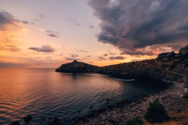 dağlar ve gökyüzünde bulutlar ile denizde kırmızı turuncu günbatımı