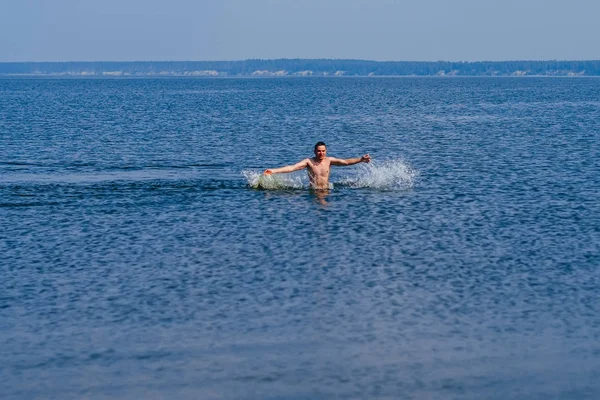 Mladý muž plave ve vodě s postřikem v létě na pláži — Stock fotografie