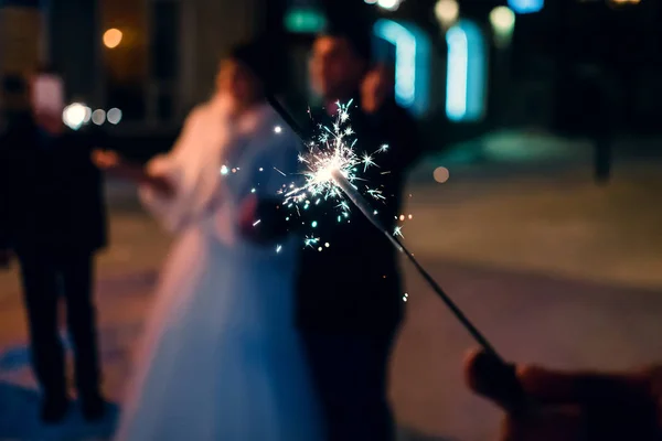 Sparkler with sparks in the hand of man on holiday on blurry background — Stock Photo, Image