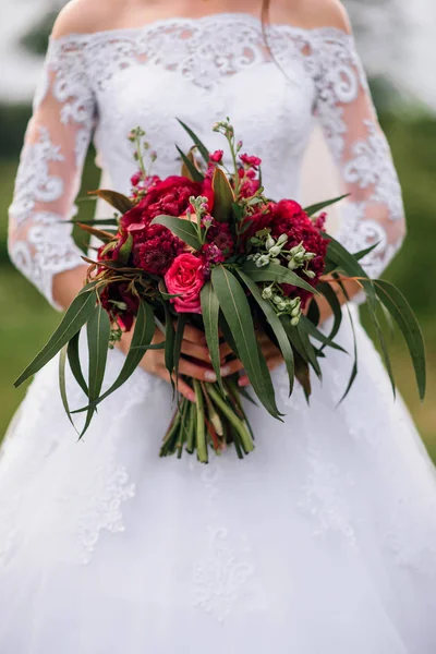 Bouquet de mariage avec pivoines rouges dans les mains de la mariée dans une robe blanche — Photo