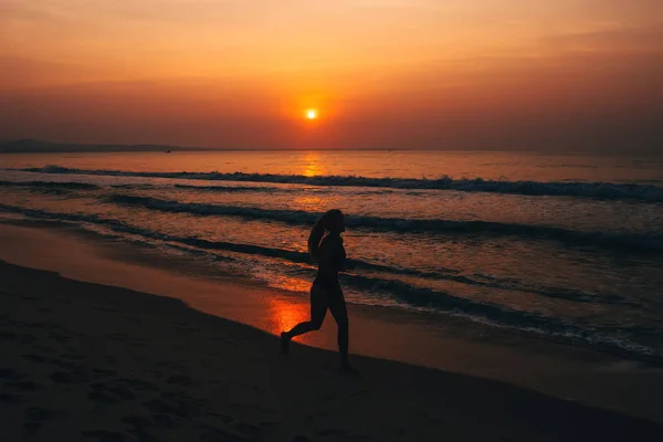 Silhouette junge Läuferin, die bei Sonnenuntergang auf dem Meer läuft — Stockfoto