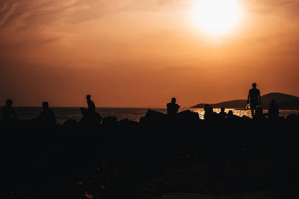 Silhouetten von Menschen, die am Strand am Meer ruhen — Stockfoto