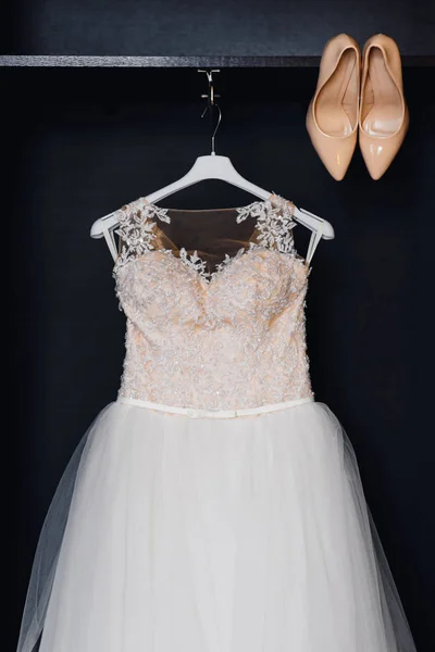 wedding white bridesmaid dress on a hanger with corset and beige shoes