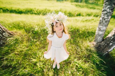 mutlu genç kız bir çelenk çiçek kafasını ve mutlu bir şekilde gülümseyerek beyaz bir elbise ile