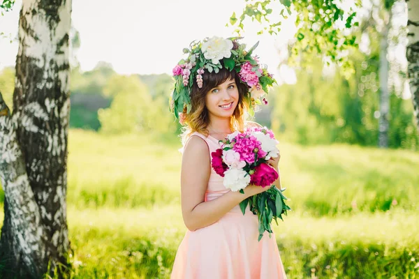 Portret van een jonge blanke meisje met een kroon op haar hoofd en een boeket van pioenrozen — Stockfoto