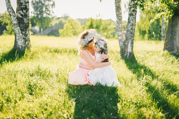 Μητέρα αγκαλιάζει την κόρη κάθεται στο γρασίδι σε εξωτερικούς χώρους σε ένα ηλιόλουστο καλοκαίρι — Φωτογραφία Αρχείου
