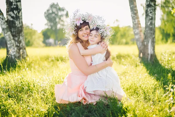 Мама обнимает свою дочь, сидя на траве на открытом воздухе в солнечное лето — стоковое фото