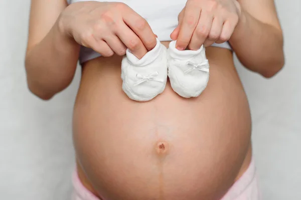 Chaussons pour nouveau-né dans les mains d'une fille enceinte — Photo