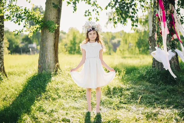 Glad ung flicka i en klänning med en krans på huvudet av blommor på fältet — Stockfoto