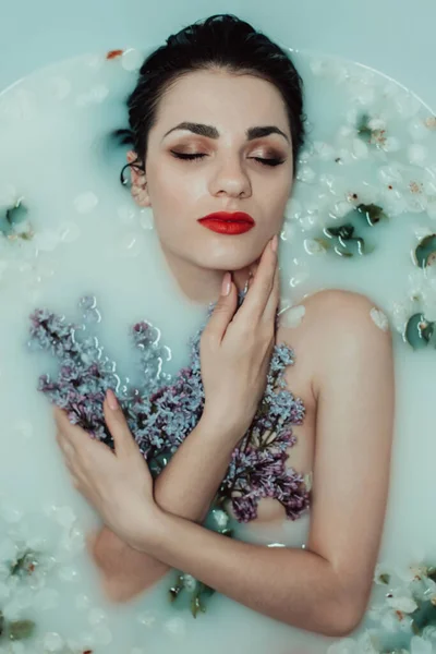 Menina nua com batom vermelho e maquiagem relaxante e descansando no banho com leite e lilás e flores de maçã — Fotografia de Stock