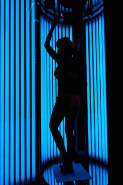 dikey solaryumda kız. Ultraviyole lambaları arka planda silüet
