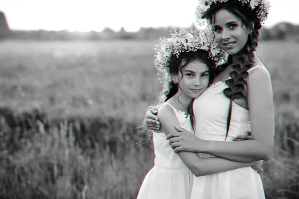 Mãe e filha abraçando juntos em vestidos brancos com tranças e coroas florais no verão — Fotografia de Stock