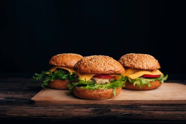 Tahta bir masada et, peynir, marul ve domatesli üç ev yapımı hamburger.