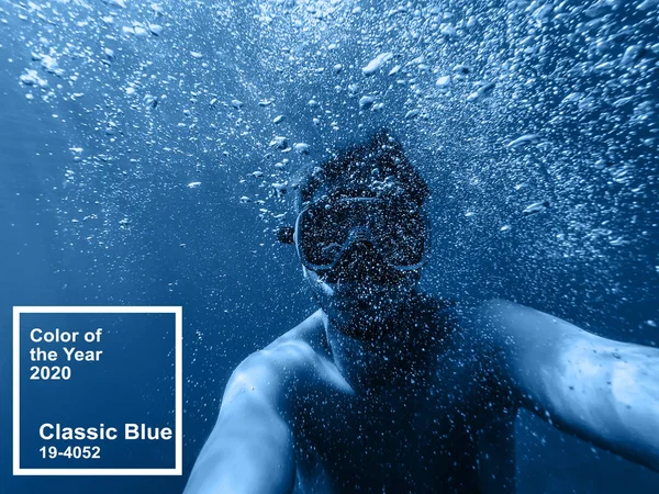 Mannelijke duiker zwemt in de zee onder water met een masker en snorkel neemt een selfie van je gezicht. Belangrijkste kleur trend 2020 klassieke blauw — Stockfoto