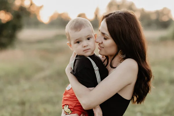 Joven madre feliz sostiene a su hijo en sus brazos en el verano —  Fotos de Stock