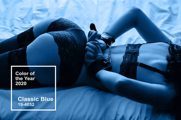 Clásico color azul del año 2020. chica en esposas de cuero acostado en la cama con un botín sexy levantado hasta — Foto de Stock