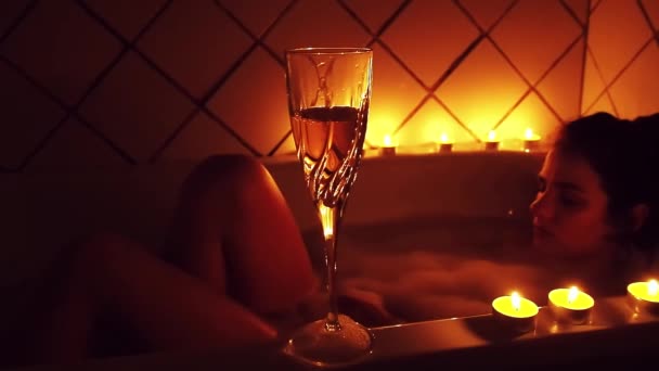 Glas Champagner mit Kerzen auf dem Hintergrund eines unscharfen entspannten jungen Mädchens im Badezimmer — Stockvideo