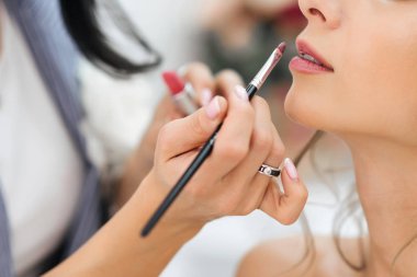 Profesyonel sanatçı makyajını yapar. Genç bir kızın yüzünde ruj izi olan bir fırçayla dudak boyar.