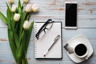 Lale kahve fincanı, smartphone ve boş defter ile ahşap arka plan üzerinde beyaz buket