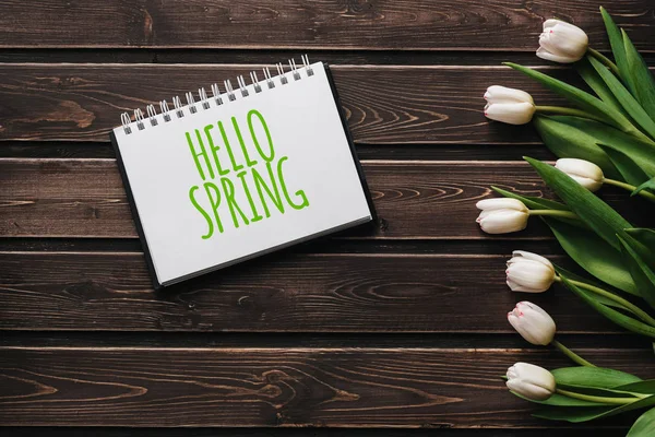 Tulipani di fiori bianchi su assi di tavolo marroni di legno. Biglietto di auguri con scritte Ciao Primavera — Foto Stock