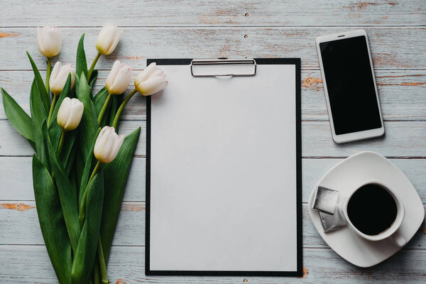 White Tulip bouquet on wooden blue background with coffee Cup, smartphone and blank paper tablet