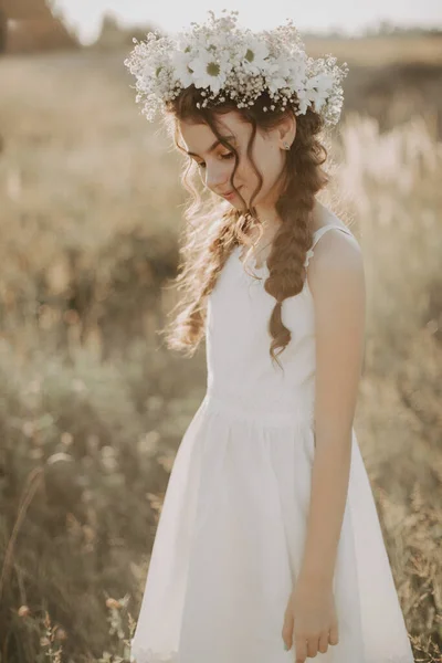 Jovem menina em um vestido branco e uma coroa de flores no verão no campo — Fotografia de Stock