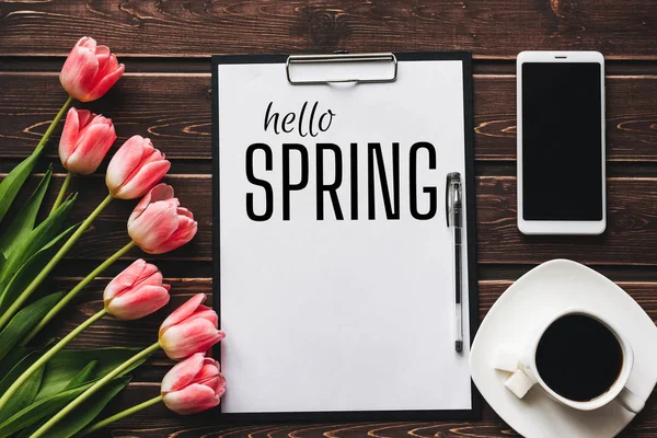 Biglietto di auguri con l'iscrizione Hello Spring. Bouquet di tulipani rosa e una tazza di caffè con uno smartphone — Foto Stock