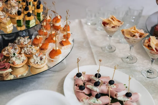 Канапе с беконом, оливками, сыром, огурцом и красной рыбой на праздничном столе в ресторане — стоковое фото