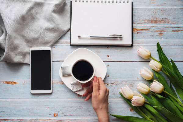 bouquet of white tulips with a Cup of coffee in womens hands, a smartphone and an empty notebook for text