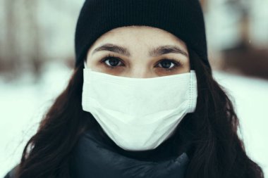 Salgın sırasında virüse karşı korunmak için tıbbi maske takan beyaz bir kızın portresi.