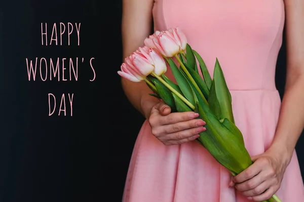 Μπουκέτο λουλούδια από ροζ τουλίπες στα χέρια ενός κοριτσιού. Ευχετήρια κάρτα με κείμενο Happy Womens Day — Φωτογραφία Αρχείου