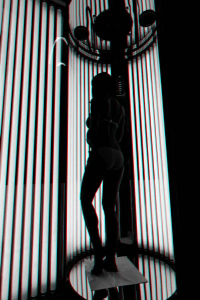 Meisje in de verticale solarium. Silhouet op de achtergrond van ultraviolette lampen — Stockfoto