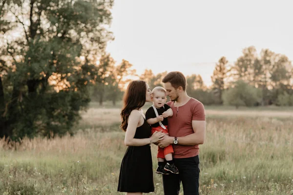 Joven mamá y papá abrazar a su hijo en verano en un campo al atardecer —  Fotos de Stock