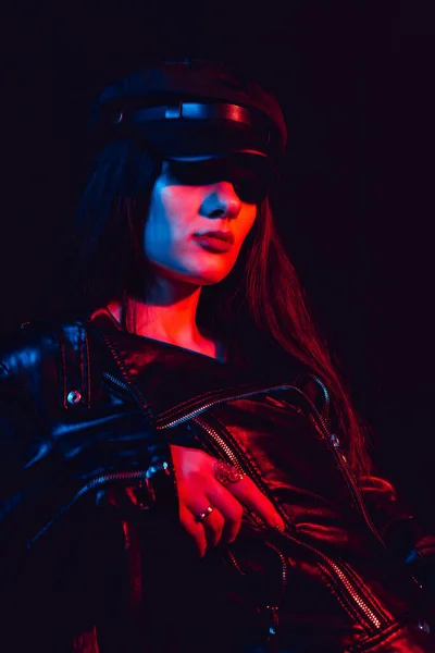 Fashionable portrait of a young sexy girl in a leather jacket and cap with a neon light — Stock Photo, Image