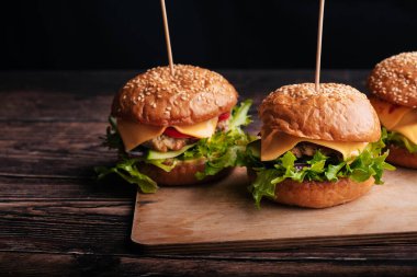 Üç ev yapımı hamburger et, peynir, marul ve domates.