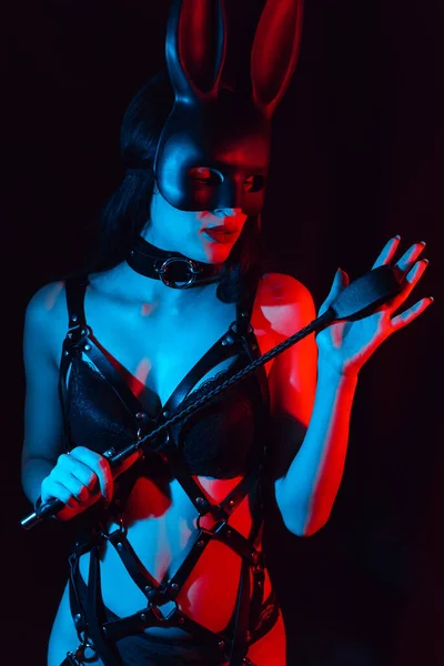 Sexy girl mistress in leather harness and Bunny mask holds a Flogger whip — Stock fotografie