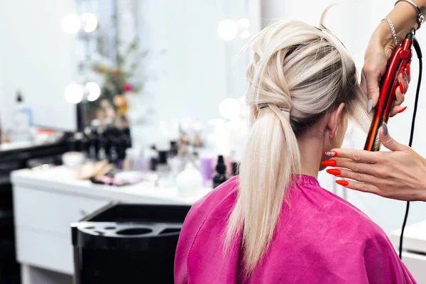 금발의 소녀는 다리미를 한 스타일리스트에 의해 머리를 깎는다 — 스톡 사진