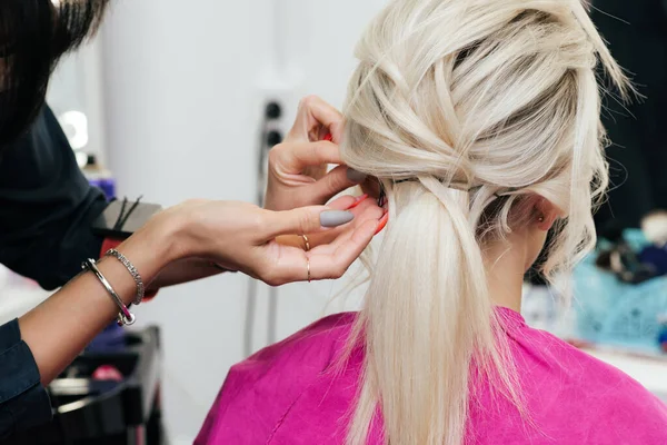 Mãos de um cabeleireiro com um grampo de cabelo invisível fazer o cabelo de uma menina loira com cabelos longos — Fotografia de Stock