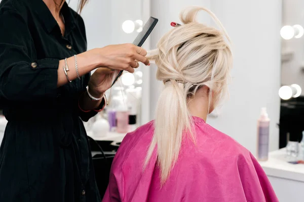 Manos de un estilista hacer un peinado para una chica rubia — Foto de Stock
