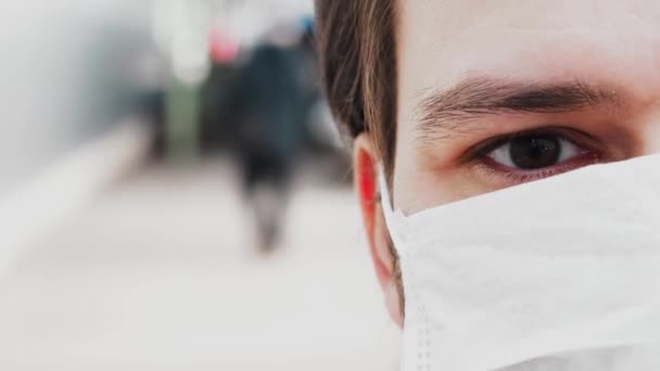 Blinkande öga med en reva av en man i en medicinsk mask för att skydda mot COVID-19 coronavirus — Stockvideo