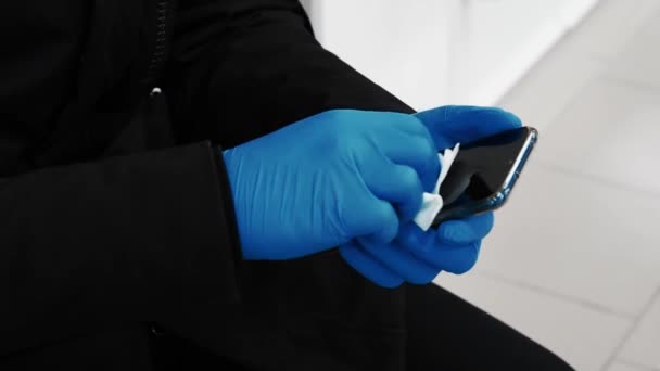 Concept van de COVID-19 coronavirus epidemie. Een man met handschoenen veegt het scherm van een mobiele telefoon af. — Stockvideo