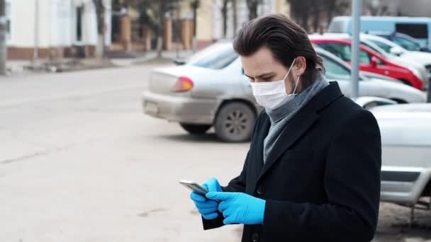 Weißer kaukasischer Mann mit Atemschutzmaske und Handschuhen zum Schutz vor dem COVID-19 Coronavirus nutzt ein Smartphone — Stockvideo