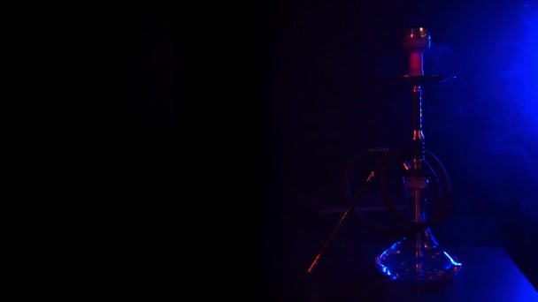 Кальян со стеклянной фляжкой с горячими углями в миске на столе с голубым дымом — стоковое видео
