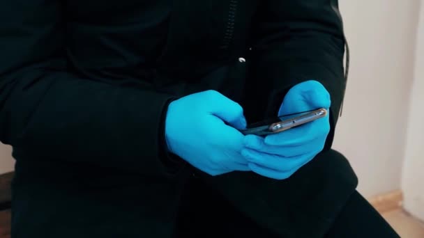 Conceito da epidemia do coronavírus COVID-19. Um homem com as mãos enluvadas usa um telefone celular — Vídeo de Stock